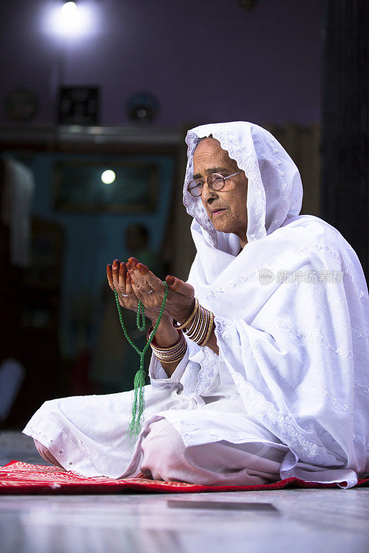 Senior Muslim Woman praying, with prayer beads beads in her hands